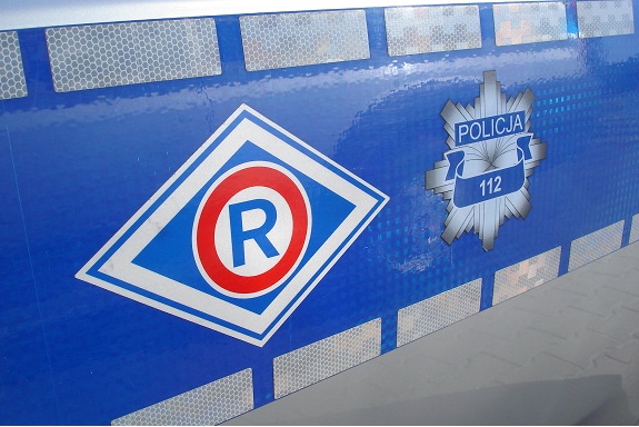 Zdjęcie dekoracyjne. Bok policyjnego radiowozu a na nim logo policji ruchu drogowego.