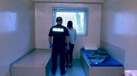 Zdjęcie przedstawiające zatrzymaną kobietę i policjanta, stojących w pomieszczeniu policyjnego aresztu.