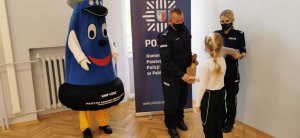Komendant Powiatowy Policji w Pabianicach gratuluje laureatce konkursu. Obok stoi policjantka i maskotka łódzkiej Policji.