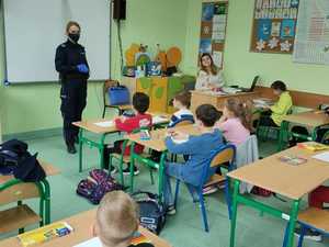 Policjantka stoi w klasie, naprzeciwko niej znajduje się grupa dzieci.
