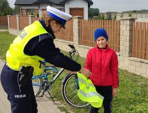 Policjantka zakładająca młodemu rowerzyście kamizelkę odblaskową.
