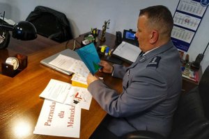 Komendant Powiatowy Policji w Pabianicach siedzi za biurkiem z kartką w rękach i czyta treść życzeń napisanych do Świętego Mikołaja.