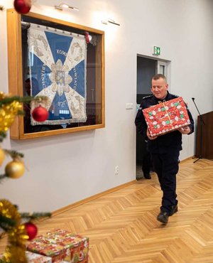 Komendant Powiatowy Policji w Pabianicach niosący prezent pod choinkę.