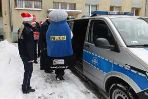 Policjanci i maskotka łódzkiej Policji wypakowują prezenty z radiowozu.