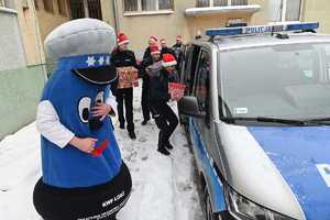 Policjanci i maskotka łódzkiej Policji wkładają prezenty do radiowozu.