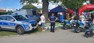 Policyjne stoisko podczas pikniku zorganizowanego przez Urząd Marszałkowski Województwa Łódzkiego. Na zdjęciu widać policyjne radiowozy i motocykle, grę wielkoformatową i granatowy namiot pabianickiej Policji.