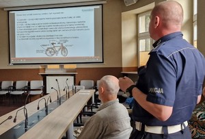 Policjant z Wydziału Ruchu Drogowego Komendy Powiatowej Policji w Pabianicach omawia prezentację, na której wyszczególnione jest obowiązkowe wyposażenie roweru.