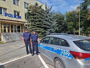 Policjanci stojący przy radiowozie na tle Komendy Powiatowej Policji w Pabianicach.