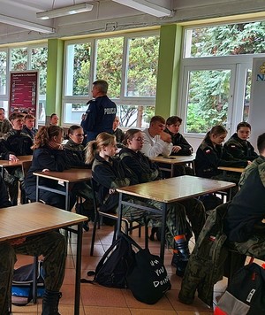 siedzący w klasie uczniowie klasy mundurowej i słuchają wykładu policjanta.