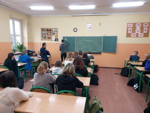 starszy sierżant Marta Bączyk prowadząca warsztaty z uczniami. Jeden z uczniów pisze na tablicy, pozostali uważnie patrzą i słuchają.
