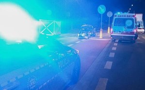 Miejsce tragicznego wypadku drogowego zabezpieczane przez Policję. Na zdjęciu widać błysk świateł policyjnego radiowozu, drogę oraz karetkę pogotowia.