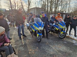 Osoby z niepełnosprawnością wsiadają na policyjne motocykle. Obok nich stoi Komendant Powiatowy Policji w Pabianicach i policjant z Wydziału Ruchu Drogowego.