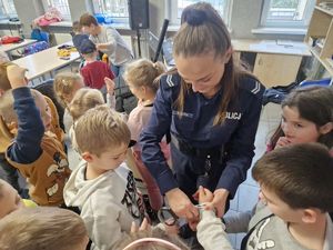Policjantka pokazuje dzieciom jak prawidłowo założyć kajdanki.