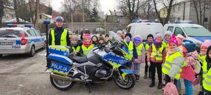 Dzieci pozują do wspólnego zdjęcia z policjantem. Wszyscy stoją przy policyjnym motocyklu.