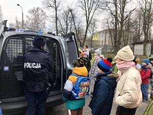 Policjantka stojąca tyłem do zdjęcia przy radiowozie razem z dziećmi.