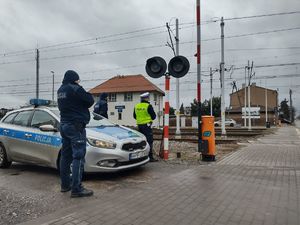 Policjanci stojący przy radiowozie obok przejazdu kolejowego.