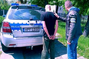 Na zdjęciu widać policjanta prowadzącego sprawcę rozboju, w tle stoi oznakowany radiowóz