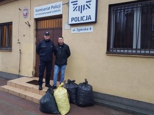 ulica przed budynkiem komisariatu, dwaj policjanci stoją przed wejściem do budynku z workami wypełnionymi nakrętkami