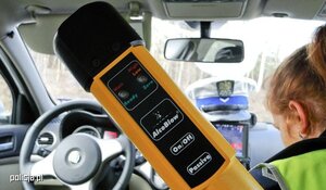 Żółty alcosensor wewnątrz radiowozu, w tle widać policjantkę.