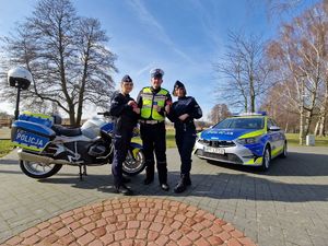 Policjantki i policjant stoją na tle radiowozu i motocykla, w rękach trzymają zawieszki w kształcie serca.