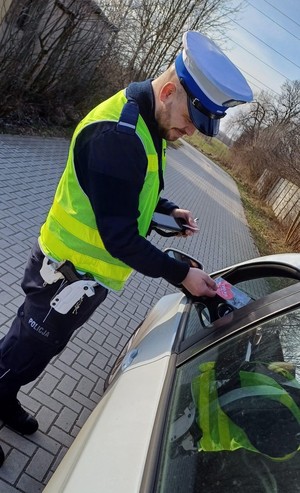 Policjant wręczający zapachową zawieszkę kierującemu.