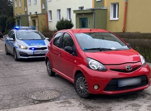 Czerwony samochód a za nim oznakowany policyjny radiowóz.