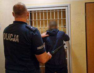 Policjant stoi przy kracie z zatrzymanym mężczyzną.