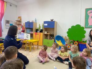Dzieci siedzą w kręgu, policjantka czyta im książkę.