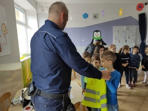 Policjant wręcza kamizelkę odblaskową chłopcu.