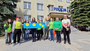 Policjantka stoi z uczestnikami gry miejskiej, w ręku trzyma niebieską makietę służącą do realizacji zadania.