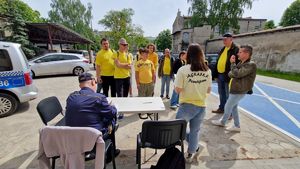 Drużyna zawodników stoi przy siedzącym strażniku miejskim, który liczy im punkty za wykonane zadanie.