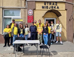 Wspólne zdjęcie uczestników i strażnika miejskiego. Wszyscy stoją przy budynku pabianickiej Straży Miejskiej.