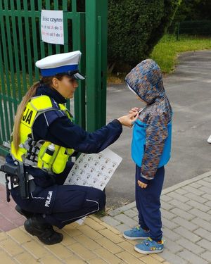 Policjantka nakleja dziecku nalepkę na kurteczkę.