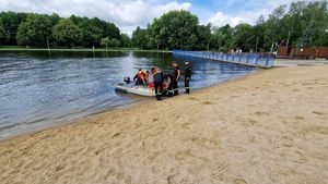 Brzeg zbiornika wodnego, strażacy są na pontonie, wyciągają z wody osobę tonącą.