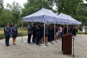 Goście i policjanci stojący pod trybuną honorową biją brawa wyróżnionym policjantom.