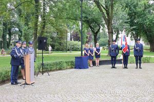 Moment, w którym Zastępca Komendanta Wojewódzkiego Policji w Łodzi stoi przy mównicy i przemawia. W tle widać policjantów, pracowników cywilnych i osoby zgromadzone na uroczystości.