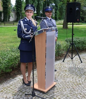 Lektor uroczystości i lektor kadrowy. Policjanci stoją przy mównicy.