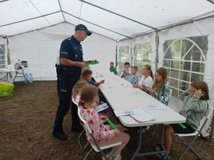 Policjant rozdaje opaski odblaskowe dzieciom.