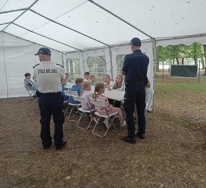 Policjant wraz ze Strażnikiem Miejskim rozmawiają z  dziećmi.