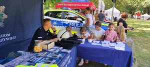 Policjant siedzi pod niebieskim namiotem i patrzy na dzieci rozwiązujące zagadki przygotowane przez stróżów prawa.