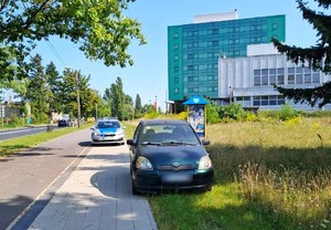 Auto zaparkowane na chodniku, w tle policyjny radiowóz i budynek sądu.