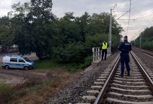 Policjant stoi na torach, w tle widać oznakowany radiowóz.