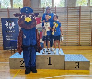 Zwycięska drużyna stoi na podium. Obok niej stoi maskotka pabianickiej policji.