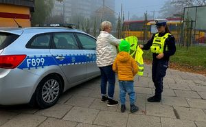 Policjantka wręcza dziecku i kobiecie kamizelki odblaskowe.