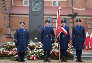 Policjanci wraz z pocztem sztandarowym stoją przed pomnikiem.