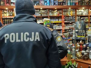 Policjant stoi w sklepie. Na półkach widać butelki z alkoholem.