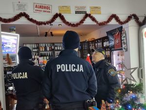 Funkcjonariusze znajdują się w sklepie. Na półkach widać butelki z alkoholem.