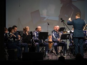 Grupa muzyków grających a instrumentach. Na pierwszym planie widać odwróconego plecami dyrygenta.