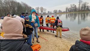 Strażacy wchodzą do wody. Dzieci przyglądają się wykonywanym przez funkcjonariuszy czynnościom.