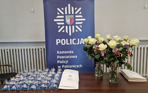 Dyplomy i upominki na tle baneru z napisem Komenda Powiatowa Policji w Pabianicach.
